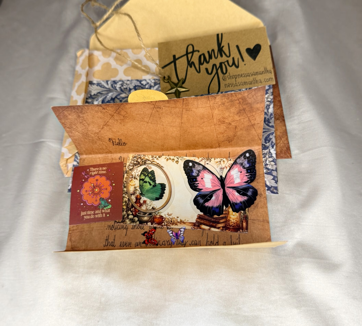 A handwritten snail mail letter from Nessa Samantha, showing stickers, butterfly charms, a blank notecard, a floral art print, and other contents.