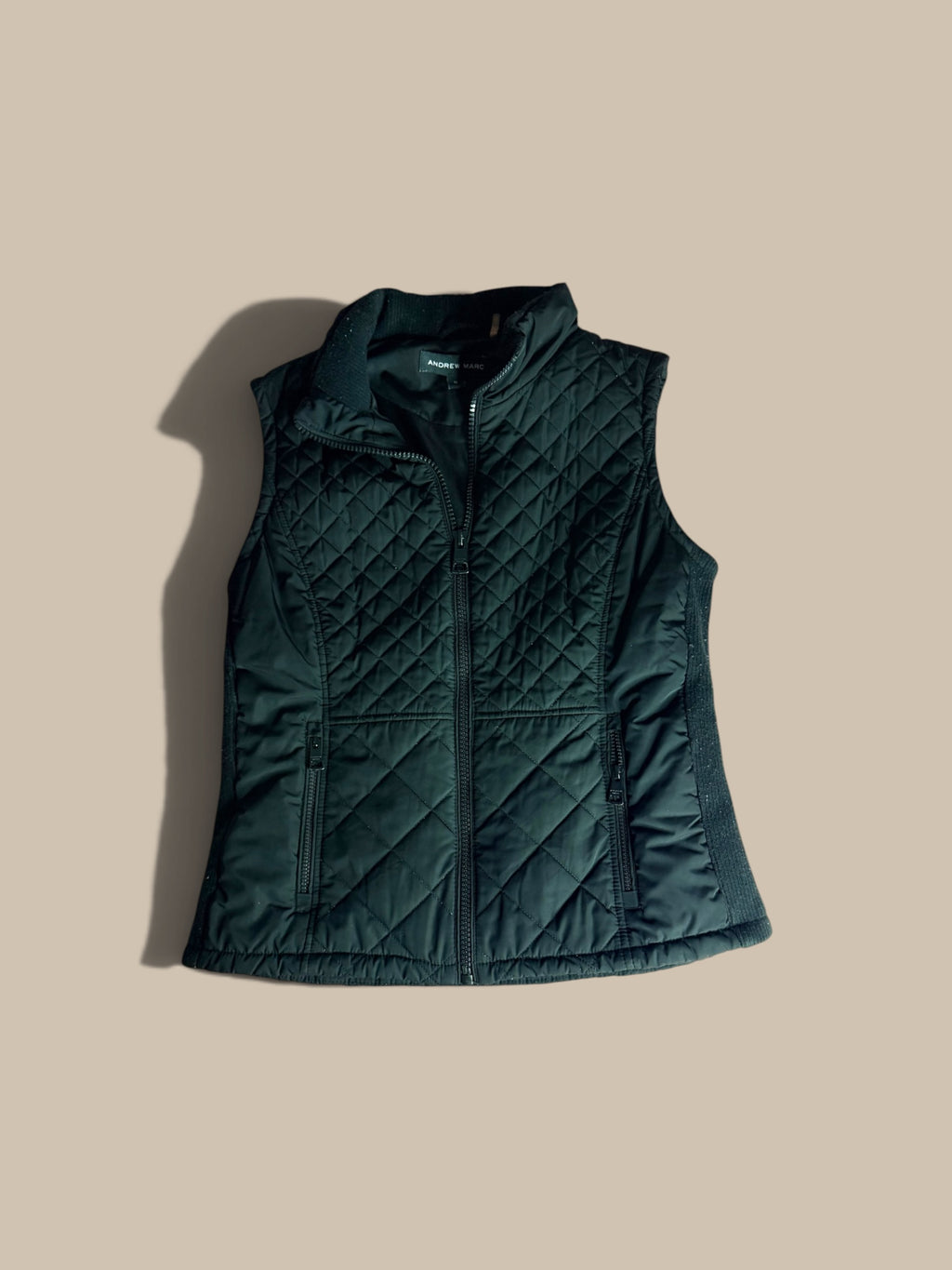 An Andrew Marc black diamond-quilted mixed-media vest with a stand collar, shown flat against a solid beige background.