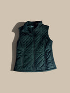 An Andrew Marc black diamond-quilted mixed-media vest with a stand collar, shown flat against a solid beige background.