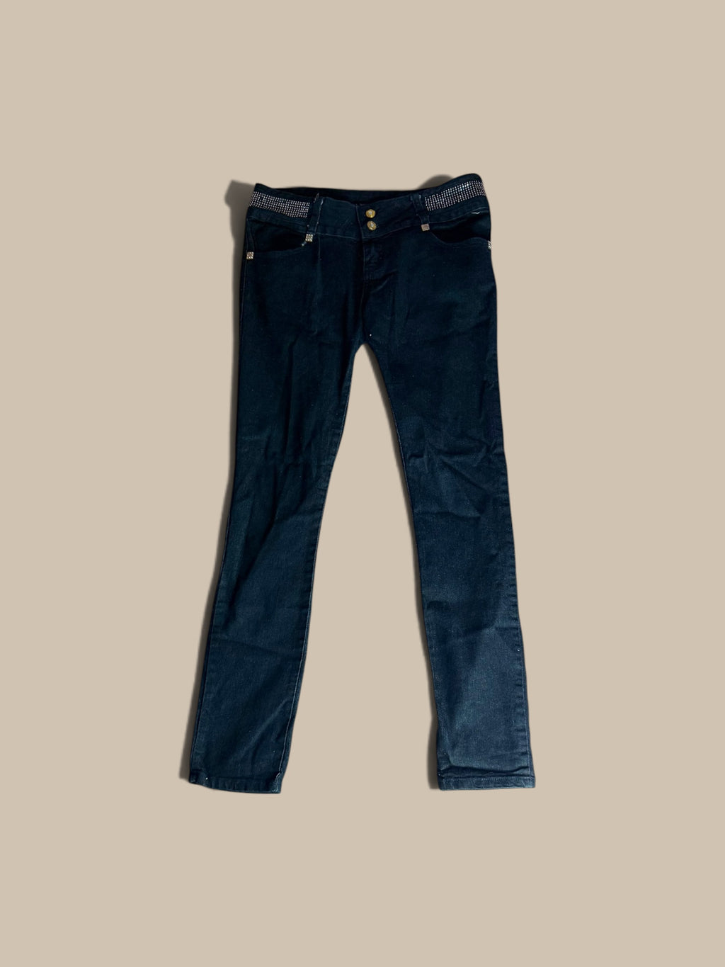 B.B. Jeans dark indigo rhinestone waistband skinny jeans laid flat against a solid beige background.
