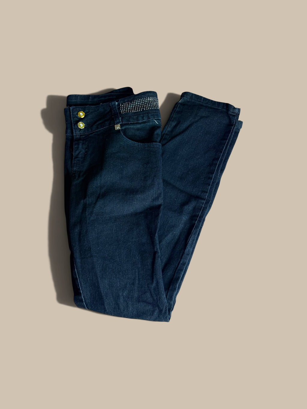A pair of dark blue B.B. Jeans skinny jeans folded neatly on a solid beige background, showing the front pocket, button closure, and waistband details.