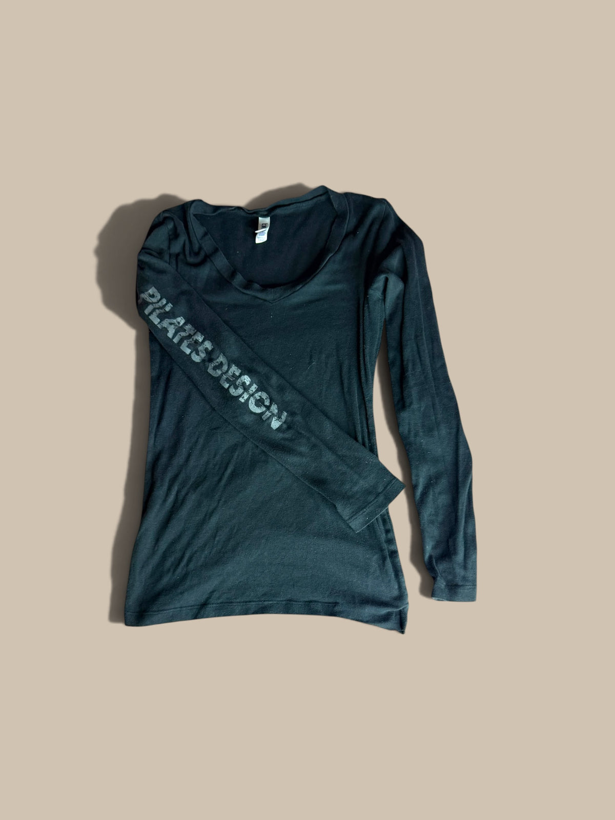 Bella Pilates Design black long-sleeve tee front flat lay with right sleeve folded across front, laid flat on a beige background.