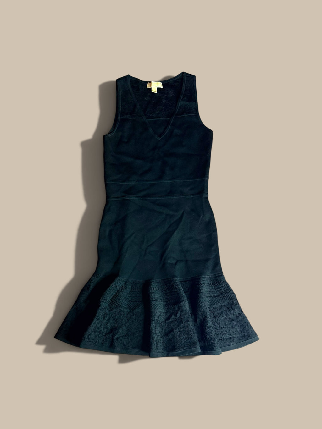 A MICHAEL Michael Kors black pointelle flounce hem knit dress front flat lay on a solid beige background.