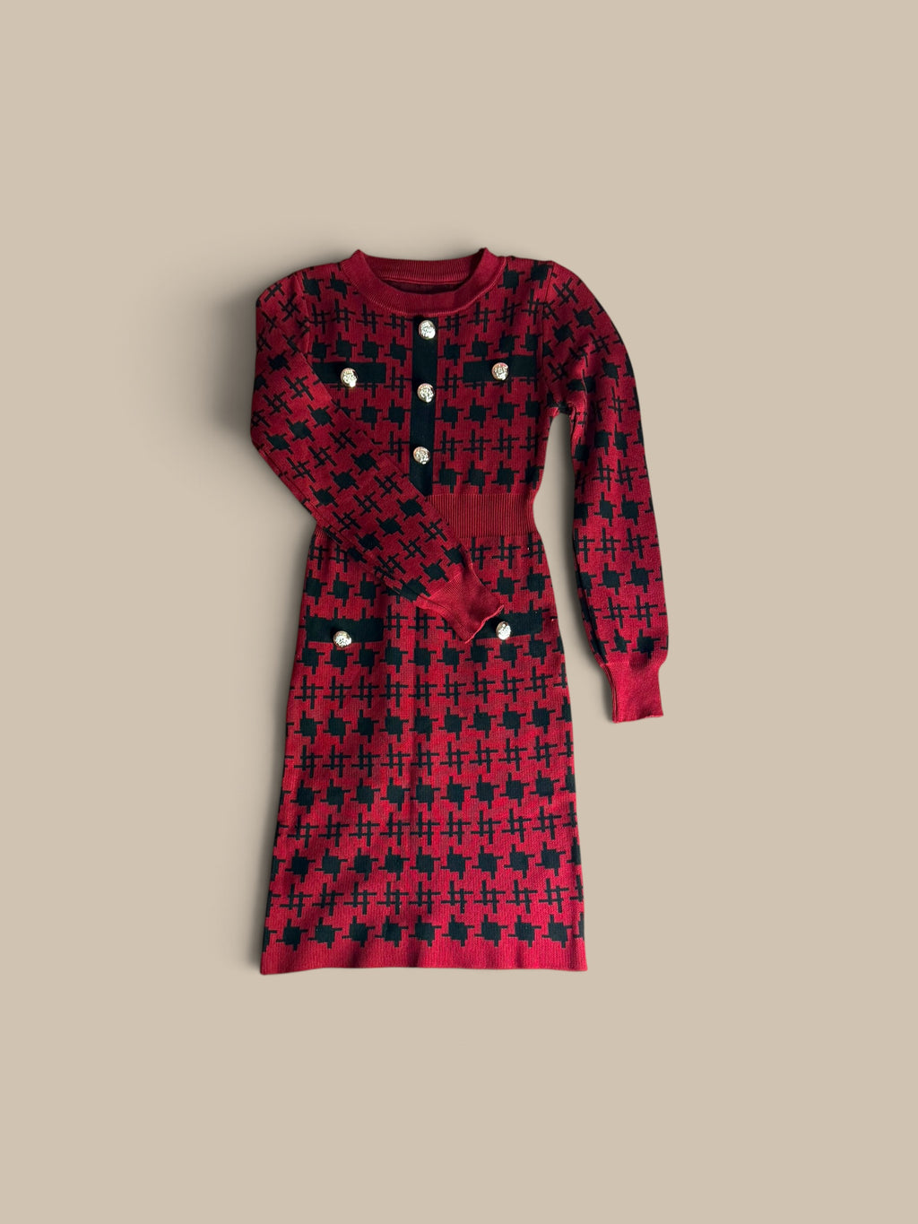 A long-sleeve Nessa Samantha crimson red and black houndstooth knit sheath dress featuring a red and black houndstooth pattern, a buttoned neckline, and front pockets with decorative buttons, laid flat on a beige background.