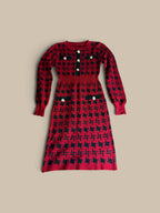 A long-sleeve Nessa Samantha crimson red and black houndstooth knit sheath dress with a red and black crosshatch pattern, laid flat on a beige background.