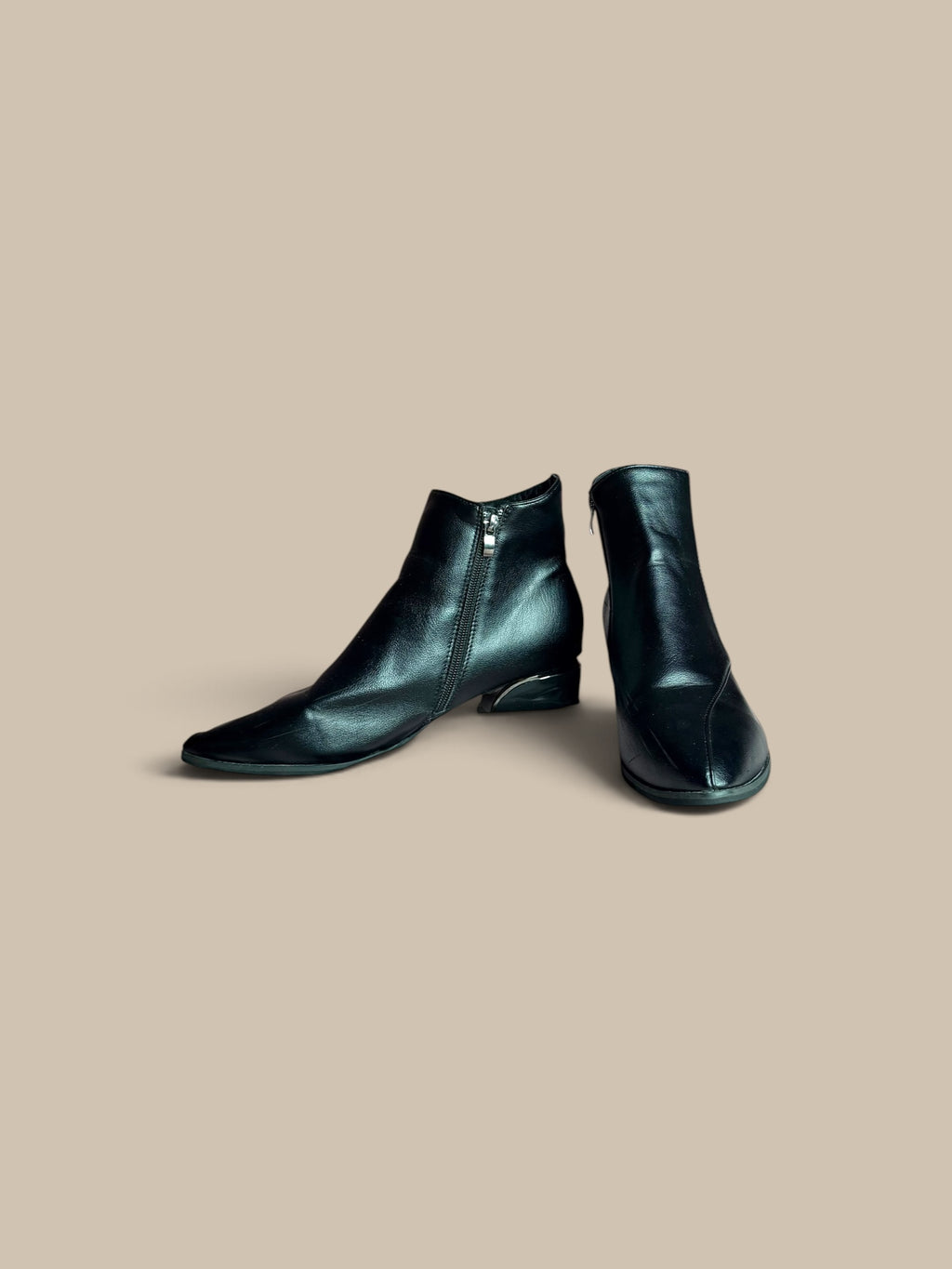A pair of Nessa Samantha black pointed-toe ankle boots with side zippers, displayed on a solid beige background.