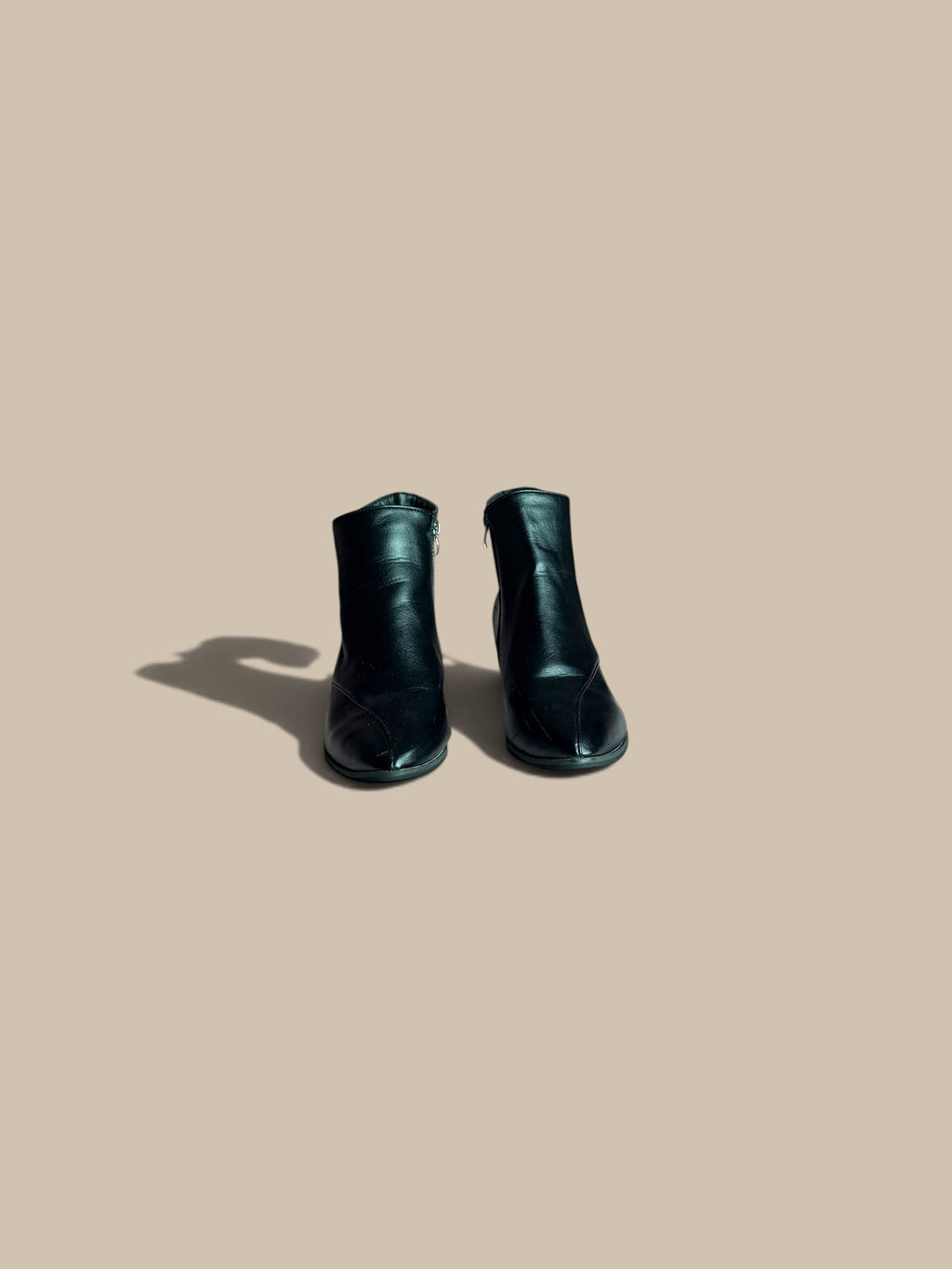 A pair of Nessa Samantha black pointed-toe block heel ankle boots forward-facing product view, shown from a high angle on a solid beige background with a soft shadow.