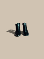 A pair of Nessa Samantha black pointed-toe block heel ankle boots forward-facing product view, shown from a high angle on a solid beige background with a soft shadow.
