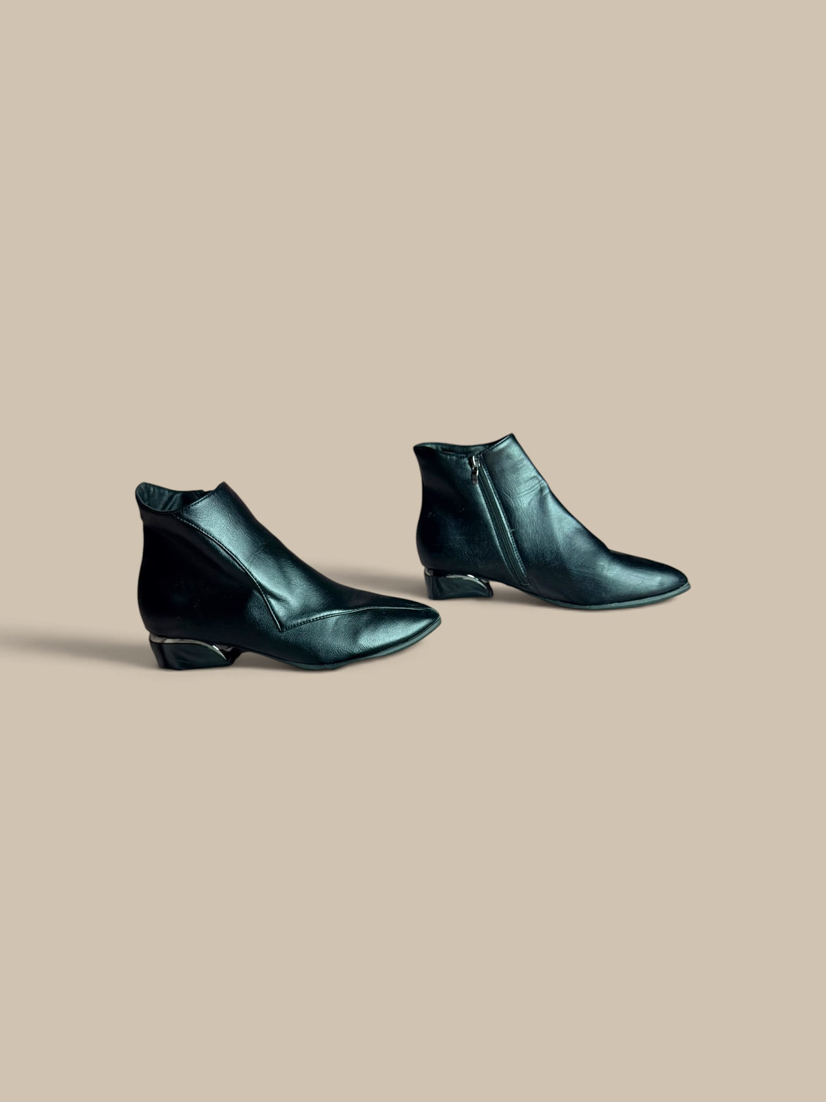 A pair of Nessa Samantha black pointed-toe ankle boots, displayed on a solid beige background.