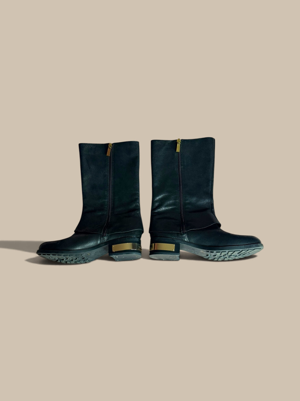 A pair of Vince Camuto Winxie black leather moto boots showing inner zipper sides against a solid beige background.