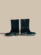 A pair of Vince Camuto Winxie black leather moto boots showing inner zipper sides against a solid beige background.