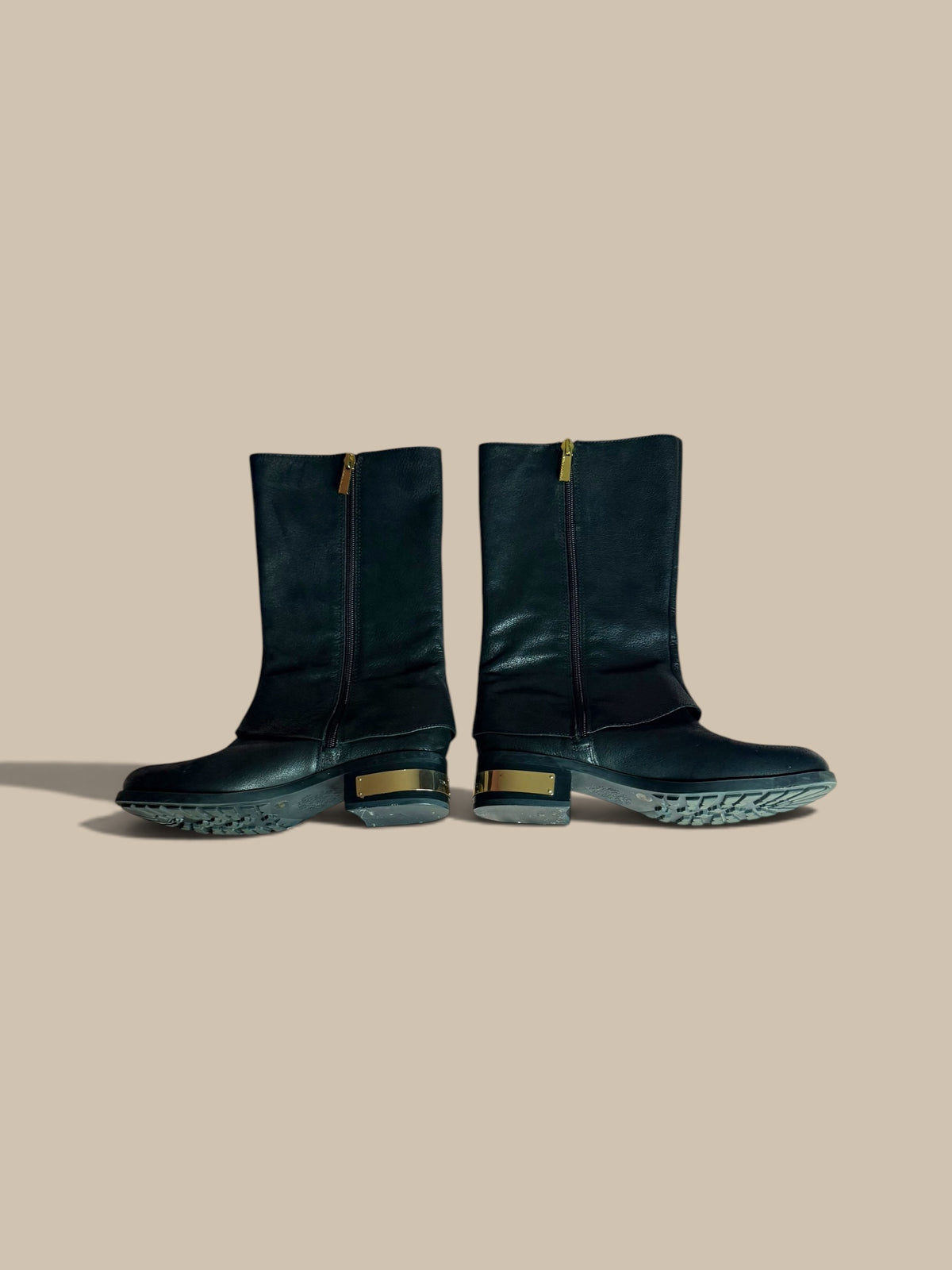 A pair of Vince Camuto Winxie black leather moto boots showing inner zipper sides against a solid beige background.