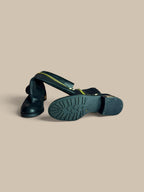 A pair of Vince Camuto Winxie black leather moto boot showing lugged sole and naturally folded shaft, shown on a solid beige background. One boot is standing upright while the other lies on its side to display the treaded sole.